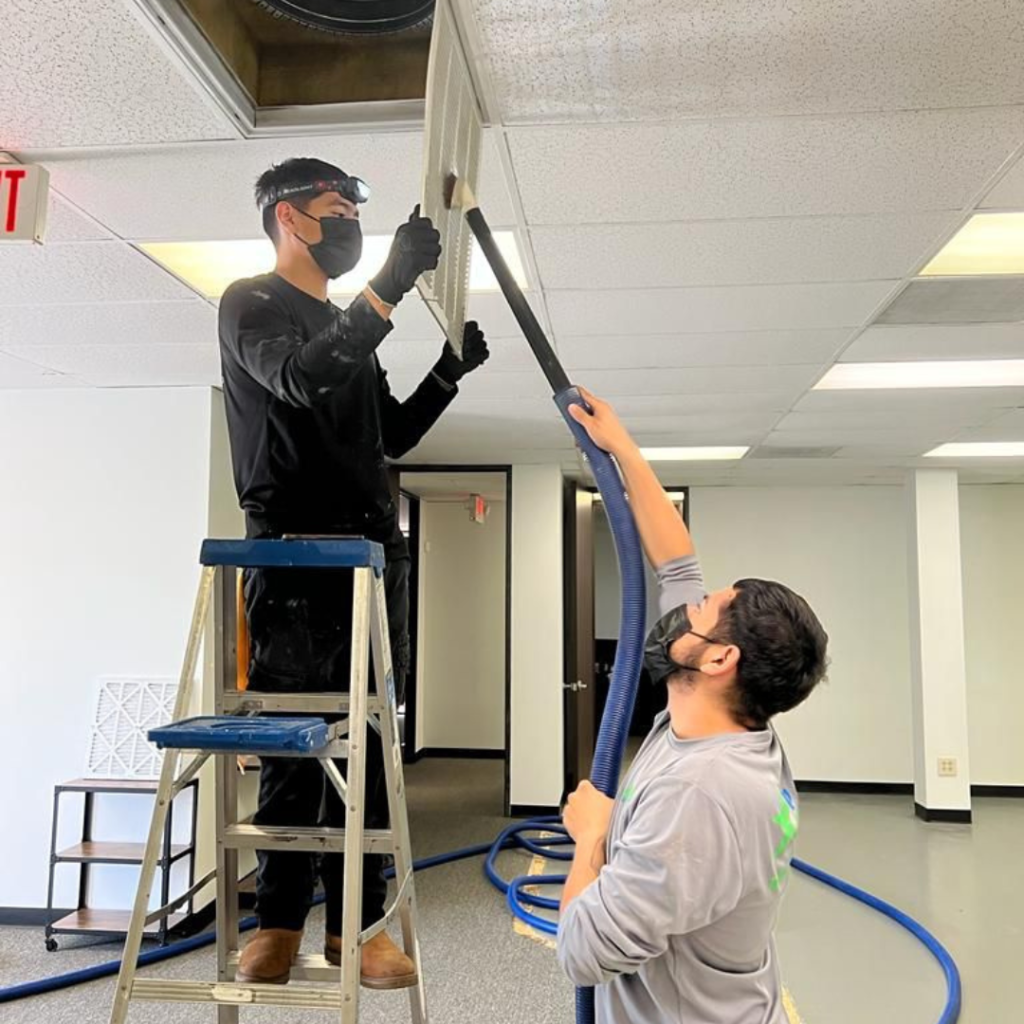 Air Duct Cleaning - Two technicians work on a ceiling fan in an office, surrounded by air duct cleaning tools working on air duct mold removal