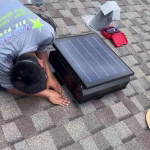 Technician installing solar attic fan on residential roof